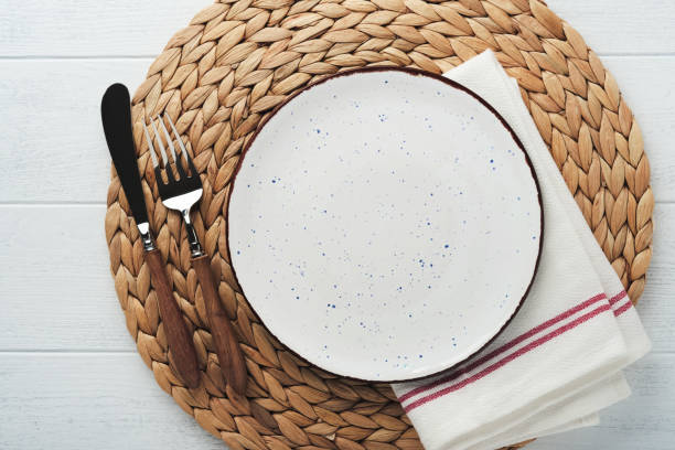 istock Vintage zero waste silverware. Rustic vintage set of white plate, wooden spoon and fork on napkin for dishes from water hyacinth on light gray concrete background. Empty dishes. Top view. Mock up. 1391058233