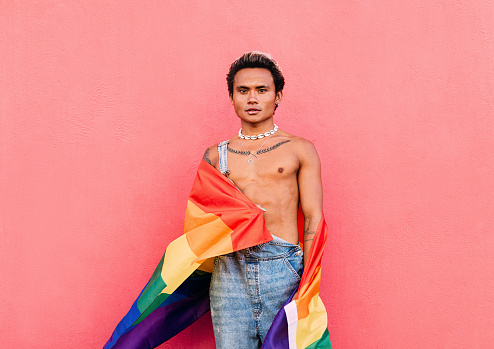 Young serious man standing outdoors with rainbow flag