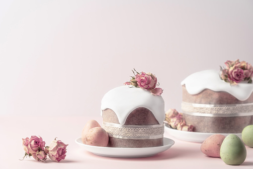 Glazed Easter cakes decorated with dry tea rose flowers on pastel pink background. Easter composition with cakes, roses and chocolate eggs. Easter background with copy space for your design.