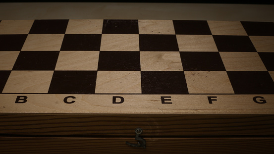 Shabby folding wooden chessboard. Playing chess with wooden lacquered pieces. Black and white squares for a sports game