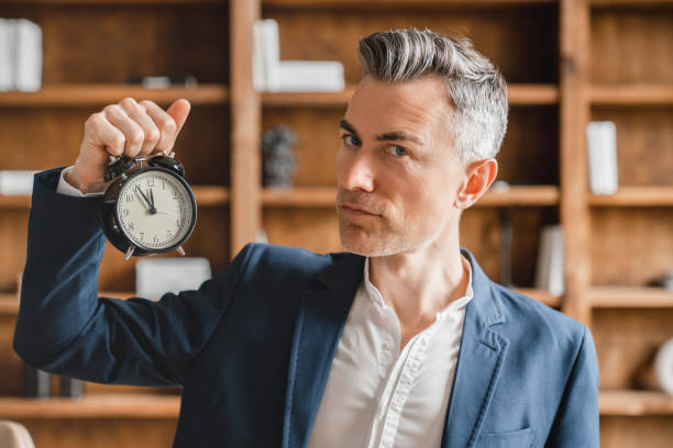 fecha tope. hombre de negocios caucásico maduro de mediana edad jefe ceo empleado independiente sosteniendo reloj reloj que muestra la hora, hora alta para la puesta en marcha en la oficina - precise timing fotografías e imágenes de stock