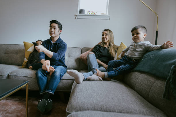 Young Family Watching Movie on Sofa A multiracial family sits down on the living room couch to watch a movie or television program together.  A fun time of relaxation and togetherness. happy indian young family couple stock pictures, royalty-free photos & images