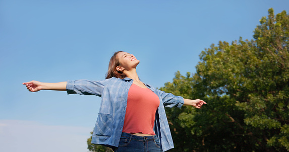 a happy asian girl outside with arms stretched up and face up with closed eyes
