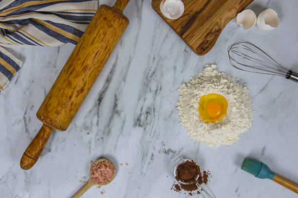 Flour, eggs, and butter are arranged on a table as dough is rolled out for Christmas cookies. Festive cookie cutters and other baking tools suggest a cheerful holiday atmosphere in the kitchen.