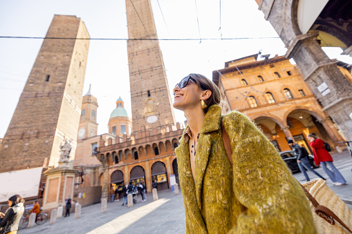 Stylish woman walks the street on background of famous towers in Bologna city. Italian lifestyle and street fashion concept. Idea of traveling Italy