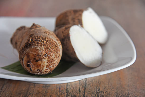 Boiled, cooked taro fruit, placed on white plate on brown wooden background