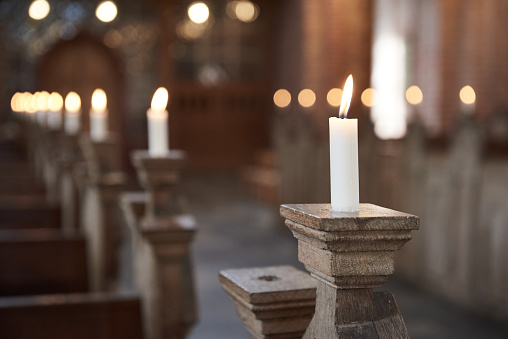 Close-up of candles burning on wooden pews in a row at illuminated church