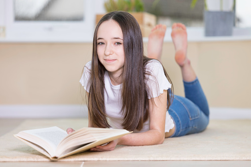 Thirteen year old girl with long brown hair reading a book.