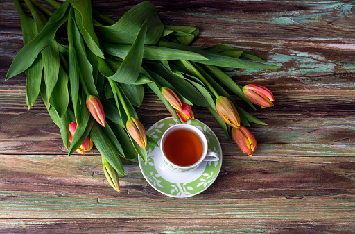 Composition for Valentine's Day, Women's Day or birthday. Romantic bouquet of red tulips and a cup of tea on a wooden background close-up.