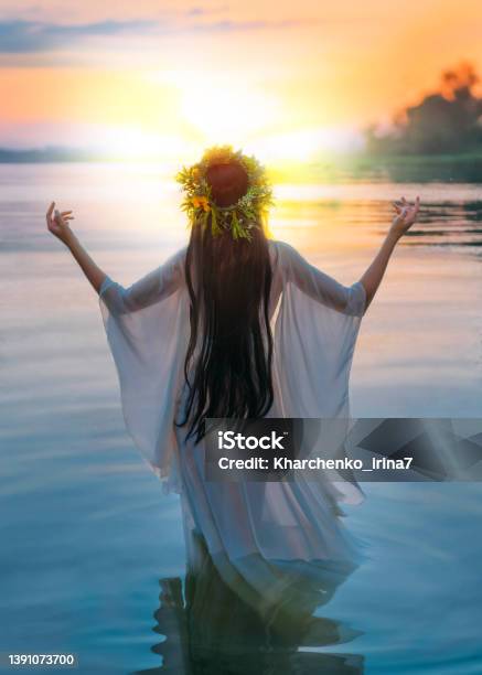 Photo With Noise Fantasy Woman Standing In Water Hands Raised To Sky Praying To Sun Slavic Girl In Herbal Wreath Long Hair White Dress Pagan Divination Ritual Nature Blue River Sunset Back View Stock Photo - Download Image Now