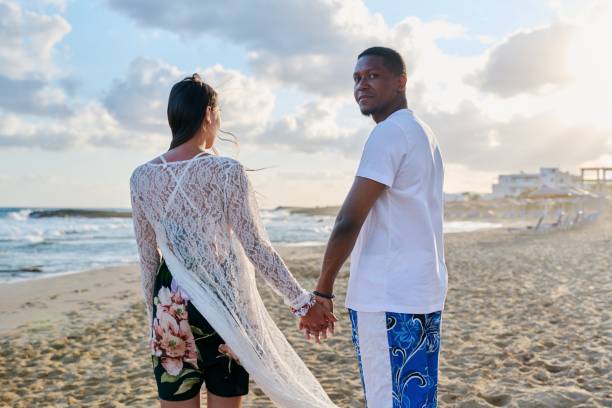 istock Young happy couple walking on the beach holding hands, back view. 1391075625