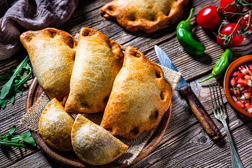 High angle view of a group of Argentinians Empanadas on a cutting board shot on rustic wooden table. High resolution 42Mp studio digital capture taken with Sony A7rII and Sony FE 90mm f2.8 macro G OSS lens