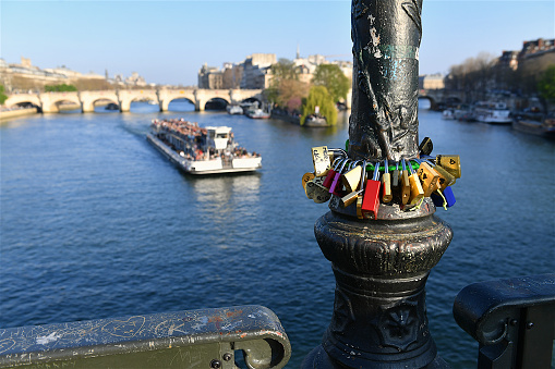 Paris, France-03 26 2022: Tour boat full of tourists on the Seine river in Paris and love locks attached to a lamppost, France.