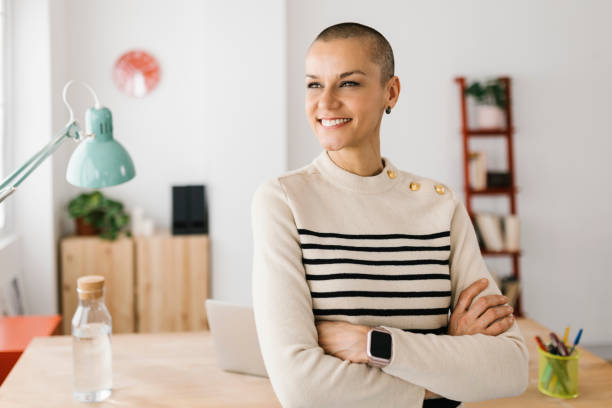 thoughtful freelance woman standing in home office - kaal geschoren hoofd stockfoto's en -beelden