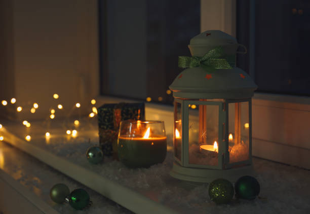 Beautiful Christmas lantern and other decorations on snowy window sill at night