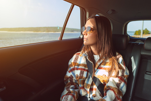 Stylish young woman sitting on back seat in the taxi car and looking through the window. High quality photo