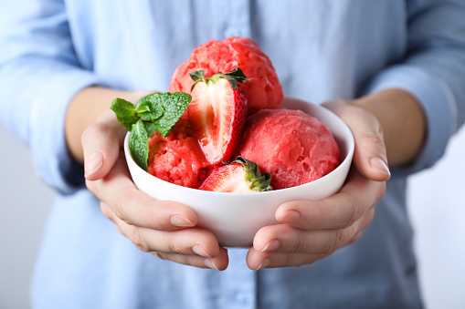 Woman holding bowl full of delicious ice cream and strawberries, closeup
