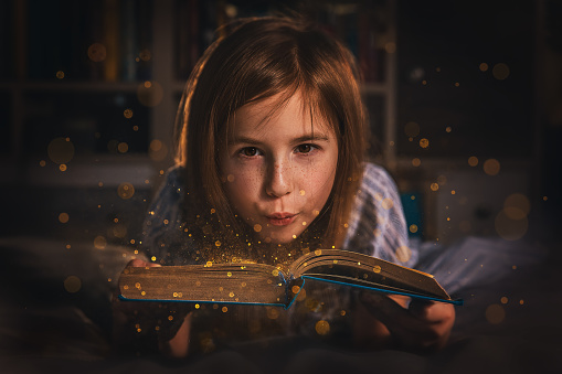 magic photo. a girl lying on the bed and blows gold dust off a book.