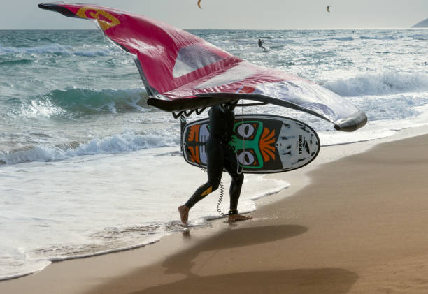 Silhouette of a person with wing foil equipment walking along the shore, a fashionable sport on the beaches, adrenaline and ecology as a hobby. Barcelona, Spain - April 8, 2022: Silhouette of a person with wing foil equipment walking along the shore, a fashionable sport on the beaches, a hobby that mixes adrenaline and ecology. kiteboarding stock pictures, royalty-free photos & images