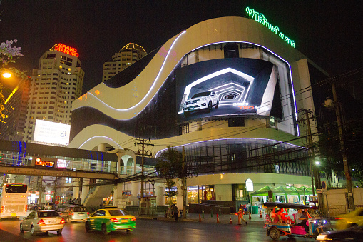 Traffic and shopping malls and skyline  at Phetchaburi Road in Bangkok at night. Some people are in scene, a tuktuk with tourists is passing street