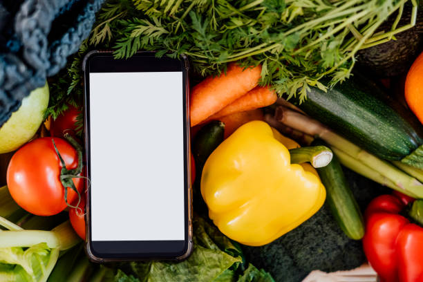 istock Top view closeup fresh vegetables and phone with blank white screen on white background. Mockup for online mobile application for diet program, food delivery, weight loss. Recipe box. Selective focus 1391094710