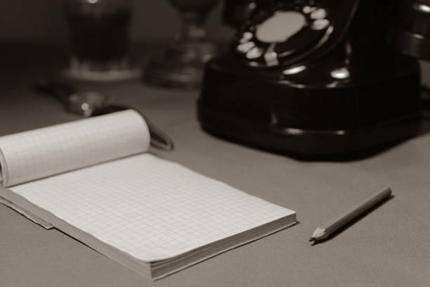 Retro notepad with a pencil for writing. Blank sheet. Wristwatch and old phone on the table. Retro composition. Black and white. Selected Focus