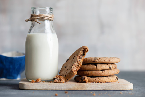 Morning breakfast of chocolate chip cookies on wooden board and glass of milk with tulle window on background. Recipe of wheat cookies with chocolate chips.