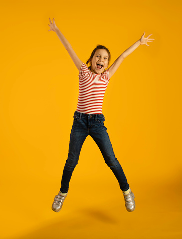 Cheerful girl jumping isolated on yellow background.