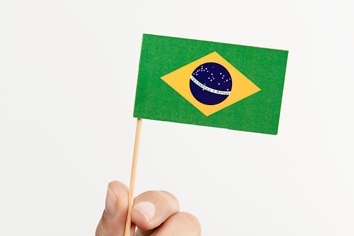 Hand is holding Brasilian flag on white background.