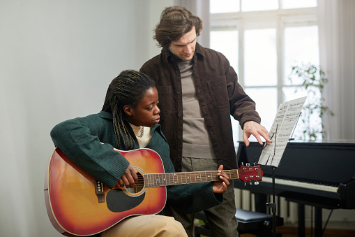 Teacher pointing at sheet music while his student learning to play the guitar during lesson