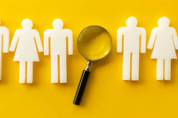 Recruitment, human resource and survey concept . Represented by a row of man and woman models in a row and one magnifying glass on yellow background.
