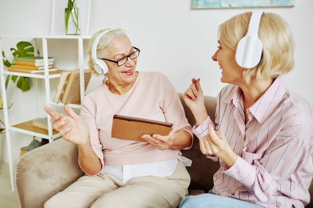 Senior Woman Listening to Music at Home Portrait of adult daughter with mother dancing together listening to music in headphones roots music stock pictures, royalty-free photos & images