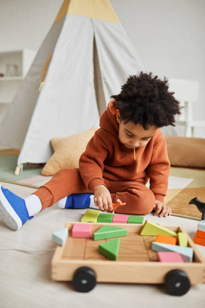 Cute African American Toddler Playing Vertical portrait of cute African American toddler playing with wooden toys in cozy kids room montessori stock pictures, royalty-free photos & images