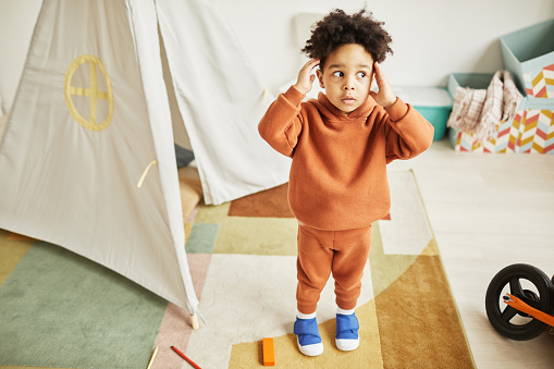 Full length portrait of cute African American toddler looking surprised and scared while playing at home and wearing minimal trendy outfit, copy space