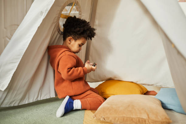 Little Toddler Playing with Smartphone Minimal side view portrait of little African American boy using smartphone in play tent and wearing trendy outfit, gen Alpha, copy space screen time and technology in babies stock pictures, royalty-free photos & images