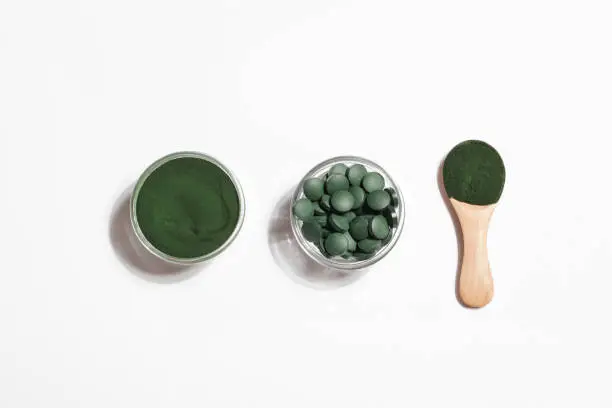 Photo of natural additives and superfood. green spirulina algae powder and pills in glass bowls on white background. healthy lifestyle concept. organic food