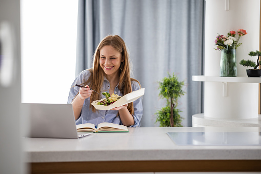 Young woman working on the laptop and eating