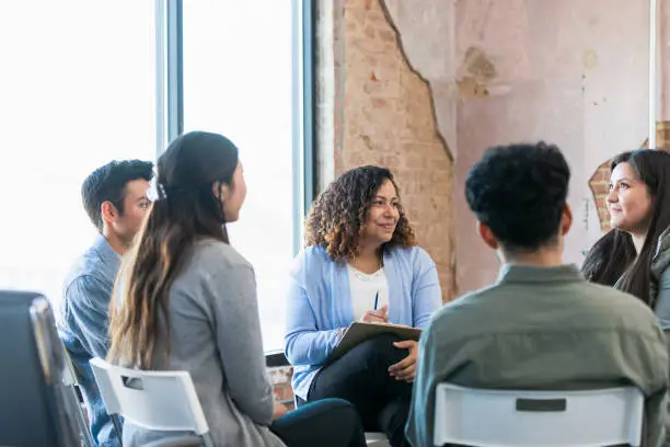 Photo of Therapy group listens attentively as young woman shares