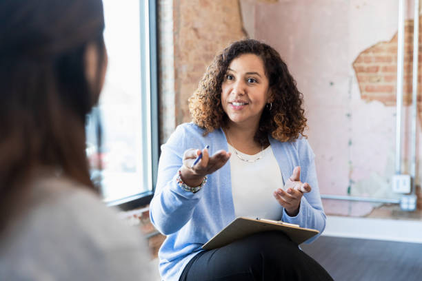 Meeting one-on-one, female therapist gestures toward unrecognizable woman Meeting with her client one-on-one, the mid adult counselor gestures toward her unrecognizable female client. explaining stock pictures, royalty-free photos & images