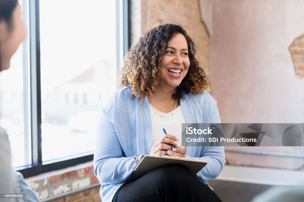 Manager smiles uncertainly at unseen team member When the unseen team member speaks, the mid adult female manager smiles uncertainly. Mental Health Professional Stock Photo