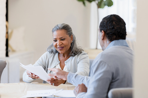 The senior adult woman smiles as the unrecognizable senior adult male insurance agent explains the paperwork to her.