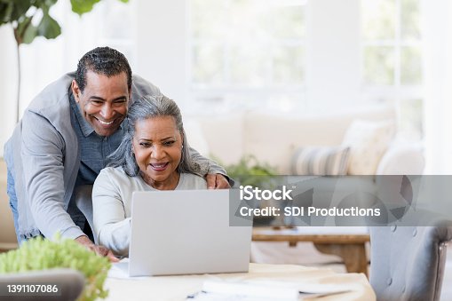 istock Husband looks over wife's shoulder at grandchildren's photos on laptop 1391107086