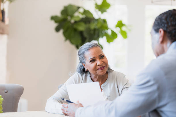 Senior widow listens to unrecognizable male financial advisor The cheerful senior adult widow listens carefully to the unrecognizable male financial advisor. independence document agreement contract stock pictures, royalty-free photos & images