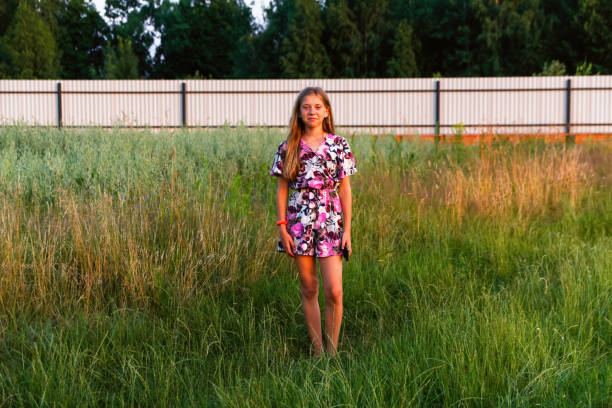 defocus beautiful smiling teenage girl in dress standing against green summer background. high girl 12 or 13 years old on summer lawn. out of focus - 12 13 years pre adolescent child female blond hair imagens e fotografias de stock