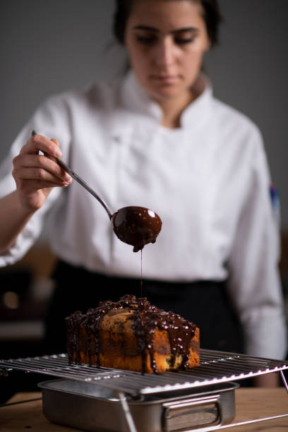Female baker pouring chocolate sauce on cake stock photo