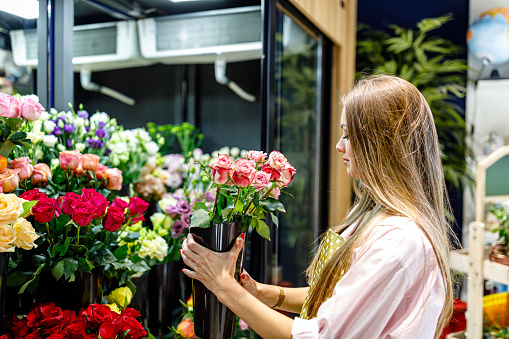 A young female florist is arranging multicolored flowers in a refrigerator in a modern flower shop.