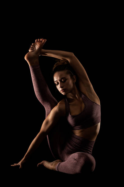 istock Fit woman practicing yoga poses. Side lit half silhouette girl doing exercise in studio against black background.. 1391119969