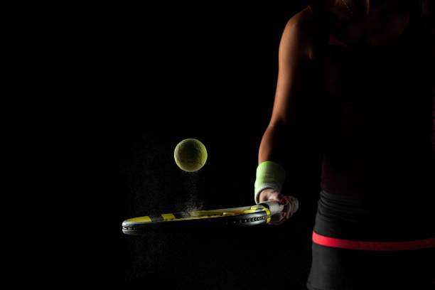 Tennis ball bouncing on racket. Dirt or magnesium dust dots visible in the air. Female player holding racket stock photo
