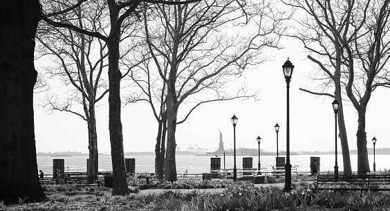 Partial view of Battery Park and the Statue of Liberty in the background photographed in black and white, NYC, USA.