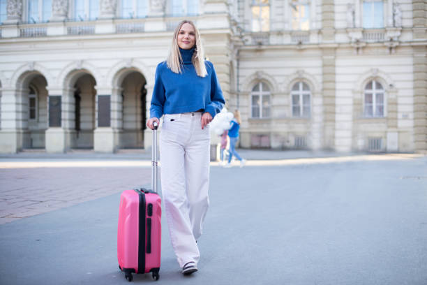 istock Young woman walking and pulling a small wheeled luggage 1391122653